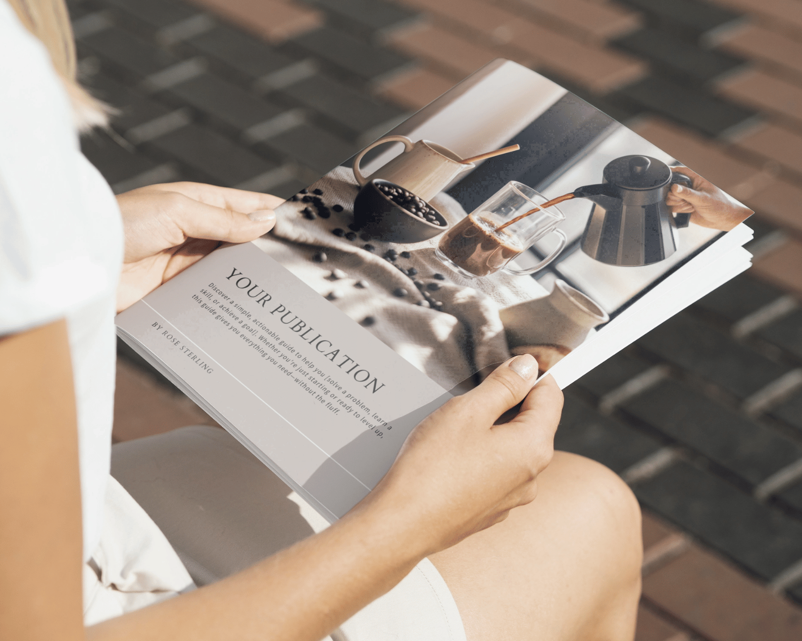 A person holds a publication featuring a coffee-themed article, with images of a kettle and beans, while seated on a brick pavement.